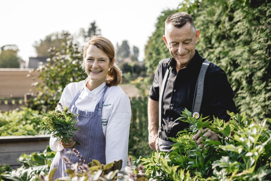 Wirtin Alexandra Labenbacher-Konecny im großen Wirtshausgarten, © Niederösterreich Werbung/David Schreiber Zwei Personen stehen in einem Garten, eine Frau in Kochkleidung hält Kräuter.