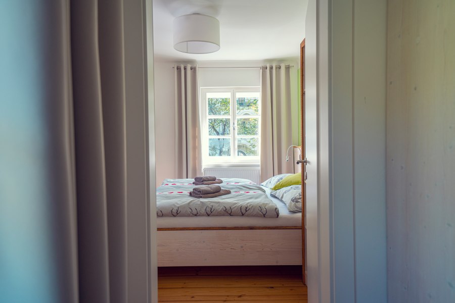 Gästezimmer, die zum länger bleiben einladen, © Schlosstaverne Lunz/Martin Stellnberger Ein gemütliches Gästezimmer mit Doppelbett, Bettwäsche mit Hirschmotiven und gefalteten Handtüchern auf dem Bett, durch eine offene Tür gesehen.