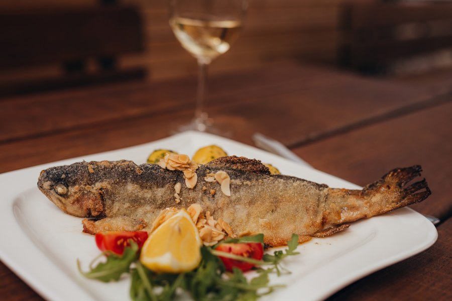 Gebratene Forelle mit Mandelbutter, © Niederösterreich Werbung/Daniela Führer Gebratene Forelle mit Mandelbutter auf einem Teller, garniert mit Zitrone und Gemüse.