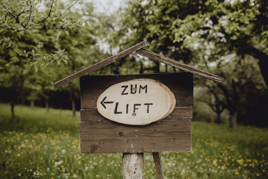 Skilift Sommer und Winter in Betrieb, © Niederösterreich Werbung/Sophie Menegaldo Holzschild im Grünen mit Aufschrift 'Zum Lift' und Pfeil nach links.