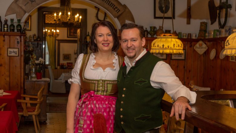 Familie Hönig, © Anton Koll Ein Paar in traditioneller bayerischer Tracht in einem rustikalen Gasthaus.