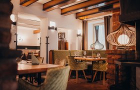 Gemütliches Ambiente bei offenem Feuer, © Niederösterreich Werbung/Daniela Führer Gemütliches Restaurant mit Holzbalken, grünen Polsterstühlen und dekorativen Lampen.
