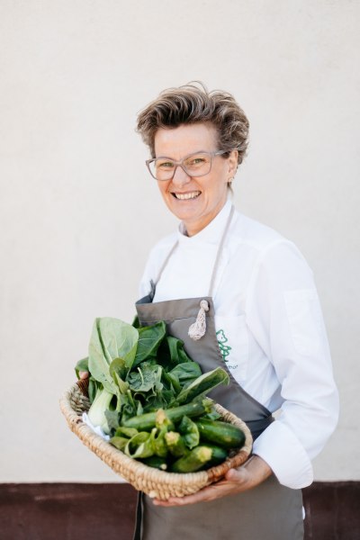 Küchenchefin Renate Schaufler, © Niederösterreich Werbung/Mara Hohla Eine lächelnde Frau in Kochkleidung hält einen Korb mit frischem Gemüse.