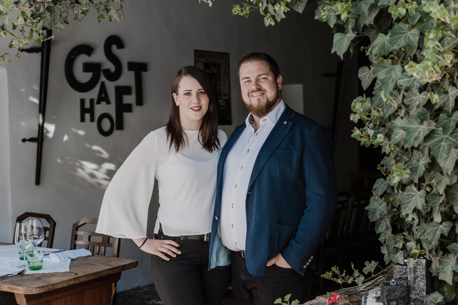 Ein Team: Matthias Strunz & Julia Hochreiter, © Niederösterreich Werbung/David Schreiber Ein Mann und eine Frau stehen lächelnd vor einem Restaurant mit dem Schriftzug 'Gasthof'.