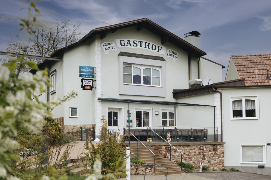 Weinviertler Wirtshauskultur, © Niederösterreich Werbung/David Schreiber Außenansicht eines Gasthofs mit Terrasse und Treppe, umgeben von Pflanzen.