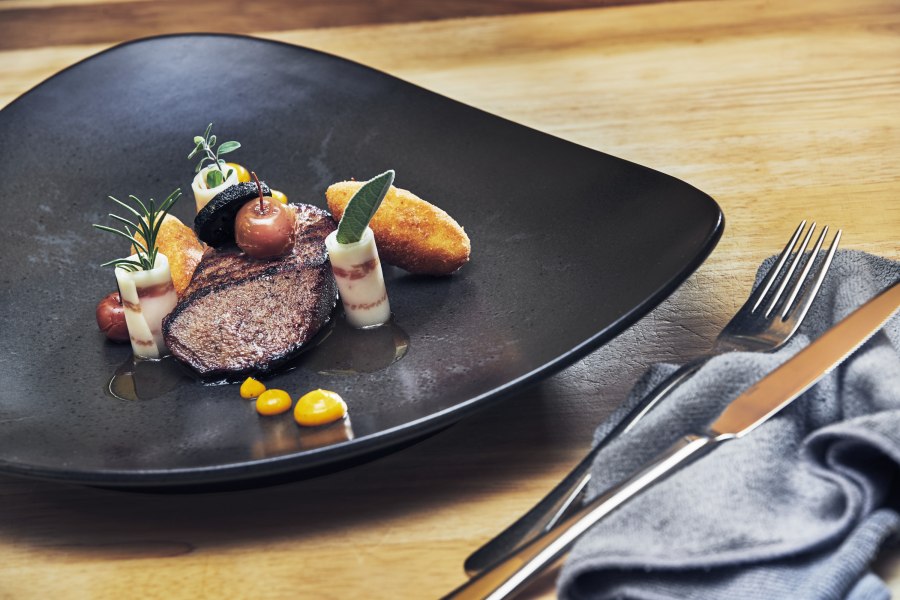 Rosa glasierte Kalbsleber, Dinkelbalsam, Mangalitza Speck, Calvados-Apferl, Polentanockerl, © Niederösterreich Werbung/Andreas Hofer Gourmetgericht mit Kalbsleber, Speck, Apfel und Polenta auf schwarzem Teller.
