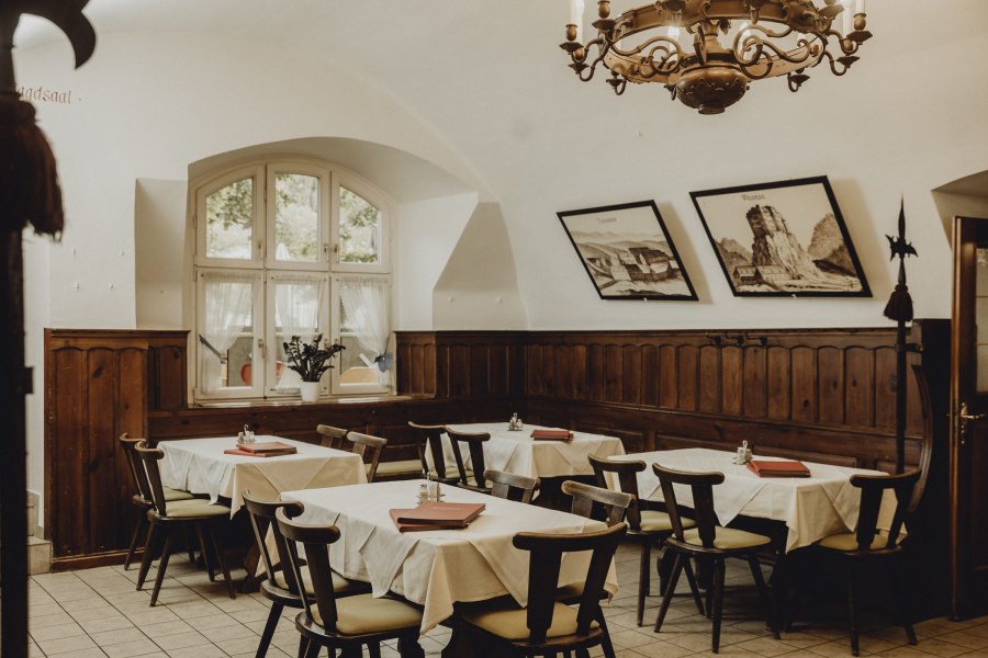 Einzigartiges Ambiente, © Niederösterreich Werbung/Sophie Menegaldo Gemütlicher Gastraum mit Holzmöbeln, weißen Tischdecken und Wandbildern.