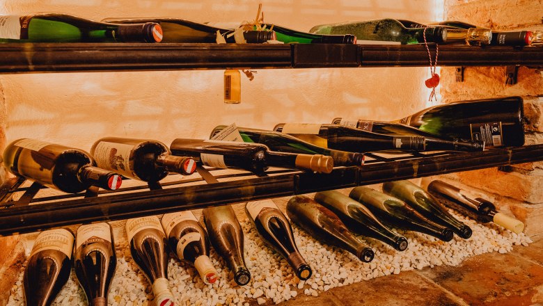 Breitgefächerte Weinauswahl, © Niederösterreich Werbung/Klaus Engelmayer Weinflaschen in einem Regal auf weißen Steinen.