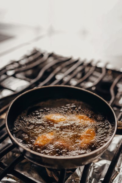 Hier wird saisonal gekocht, © Niederösterreich Werbung/Daniela Führer Nahaufnahme einer Pfanne mit kochendem Öl und frittierten Stücken auf einem Herd.