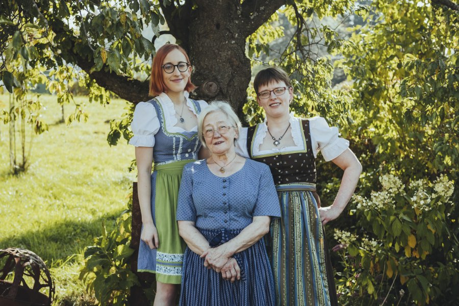 Generationsübergreifende Frauenpower, © Niederösterreich Werbung/David Schreiber Drei Frauen in traditioneller Tracht stehen lächelnd unter einem Baum im Freien.