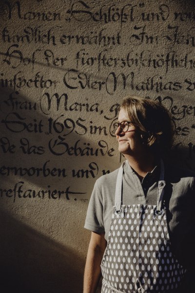 Wirtin Ruth Tastl, © Niederösterreich Werbung/Sophie Menegaldo Person mit Schürze vor historischer Wand mit alter Schrift.