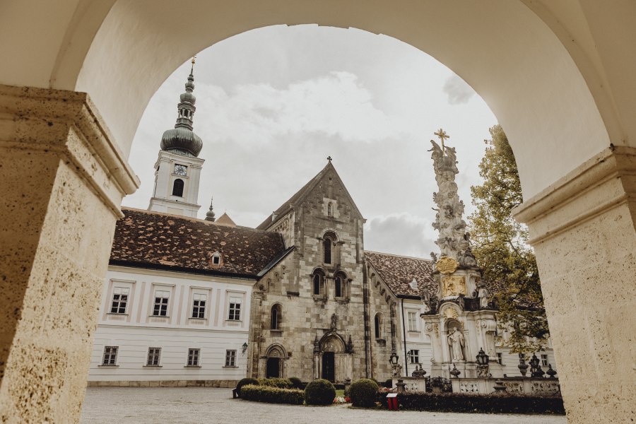 Gasthof, Stift und Klosterladen, © Niederösterreich Werbung/Sophie Menegaldo Blick durch einen Torbogen auf ein historisches Klostergebäude mit Turm und einer barocken Säule im Vordergrund.