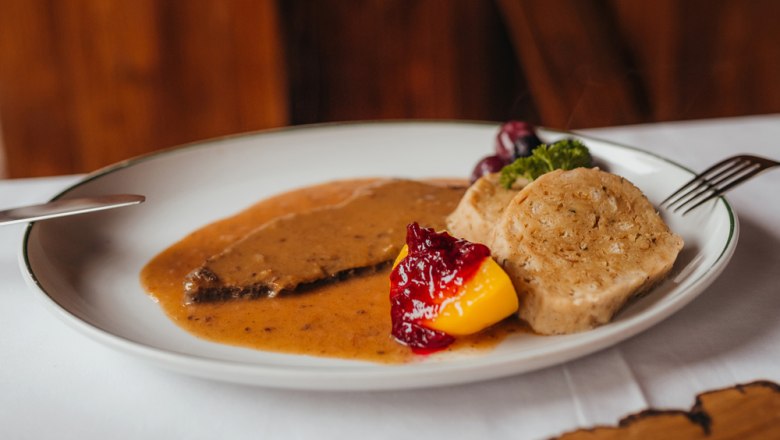 Hirschbraten mit dickem Wurzelsaft und Knödel, © Niederösterreich Werbung/Daniela Führer Ein Teller mit Hirschbraten, Knödeln, Preiselbeeren und Gemüse.
