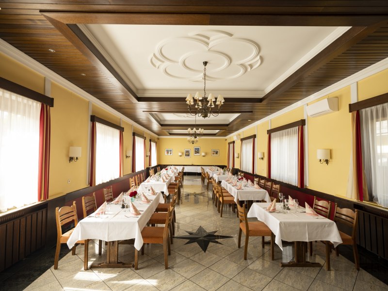 Einkehre – für Feste aller Art, © Niederösterreich Werbung/Michael Reidinger Ein festlich gedeckter Speisesaal mit gelben Wänden, Holzmöbeln und weißen Tischdecken.