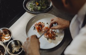 Küche: mutig, wild, regional verwurzelt, © Niederösterreich Werbung/Sophie Menegaldo Koch dekoriert ein Gericht mit Lachs und Gemüse auf einem Teller.