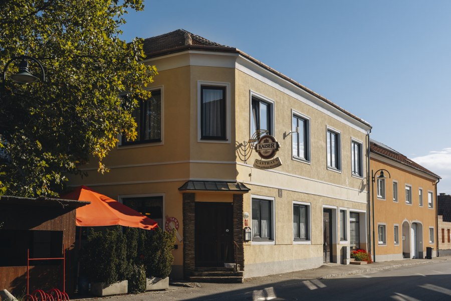 Landgasthof in Bierbaum am Kleebühel, © Niederösterreich Werbung/David Schreiber Gelbes Gasthaus mit Schild und rotem Sonnenschirm in sonniger Straße.