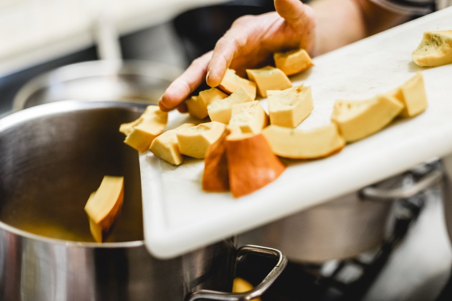 Regional-saisonale Küche, © Niederösterreich Werbung/David Schreiber Eine Hand schiebt geschnittene Kürbisstücke von einem Schneidebrett in einen Topf.