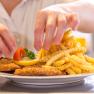 Wiener Schnitzel mit Pommes, © Foto Weidinger Ein Teller mit Wiener Schnitzel, Pommes frites, Zitrone und Tomate wird von einer Person angerichtet.