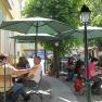 Gastgarten draußen, © Familie Frey Menschen sitzen in einem sonnigen Gastgarten mit grünen Sonnenschirmen.
