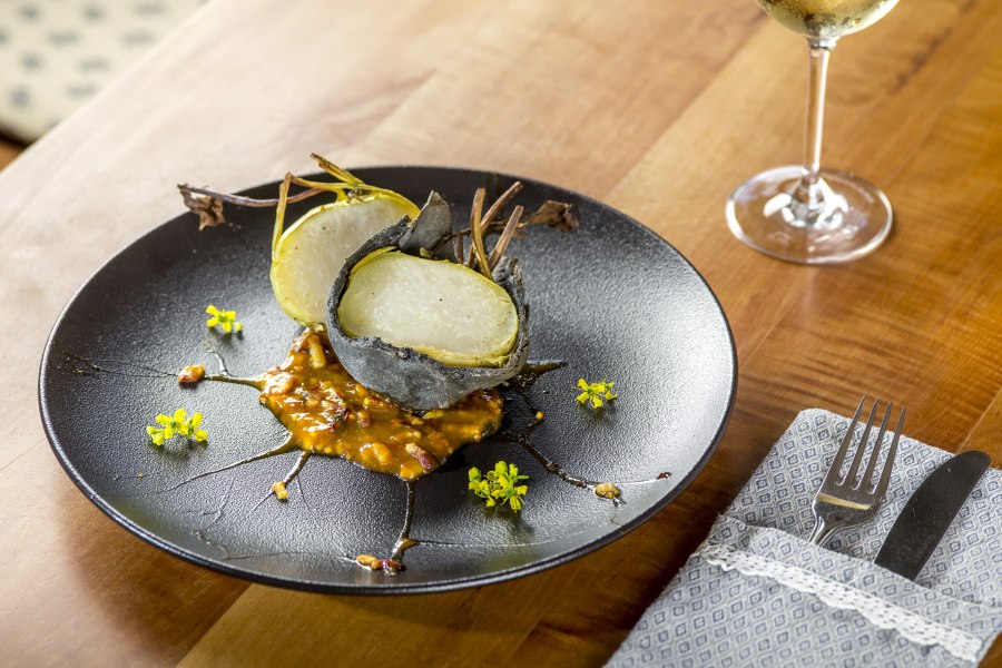 Kohlrabi in der Steinkruste auf Speckbirn-Most Marmelade, © Niederösterreich Werbung/Kurt Pinter Ein Gericht mit Kohlrabi in Steinkruste auf Speckbirn-Most Marmelade, serviert auf einem schwarzen Teller mit gelben Blüten.