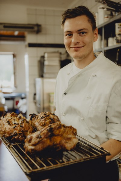 Koch Josef Fuchs setzt auf Rind, Fisch & Wild, © Niederösterreich Werbung/Rita Newman Ein Koch in weißer Uniform hält ein Tablett mit gebratenem Fleisch in einer Küche.
