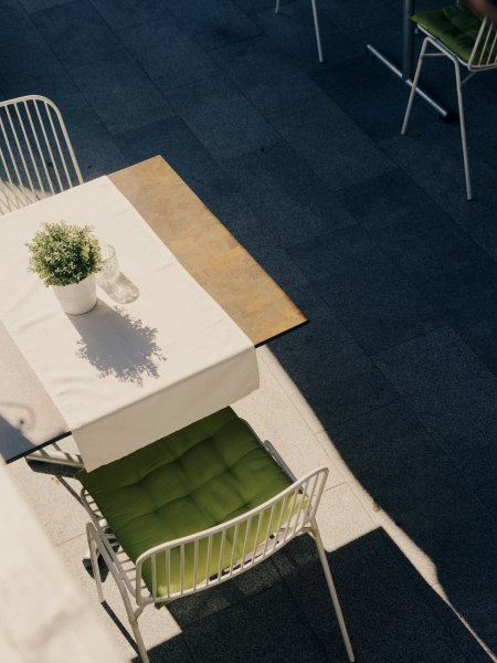 Gastgarten trifft Kräutergarten, © Niederösterreich Werbung/Julius Hirtzberger Ein Tisch mit weißer Tischdecke und Topfpflanze, daneben ein Stuhl mit grünem Kissen auf einer Terrasse.