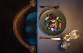 Schweinsmedaillons, Zwiebel-Most-Sauce, lila Erdäpfel, © Niederösterreich Werbung/Daniela Führer Ein Teller mit Schweinsmedaillons, lila Kartoffeln und Gemüse auf einem gedeckten Tisch.