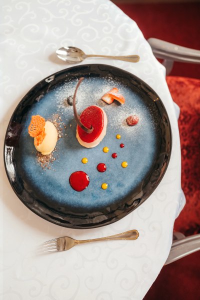 Moussetörtchen von der Ruby-Kakaobohne mit Kalamansi-Sorbet, © Niederösterreich Werbung/Daniela Führer Ein kunstvoll angerichtetes Dessert auf einem blauen Teller mit roten und gelben Saucenpunkten.