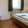Doppelzimmer, © Magdalena Donhauser Schlafzimmer mit Doppelbett, Fenster mit grünen Vorhängen, Sofa, Tisch, Tapete und einer Wandlampe.