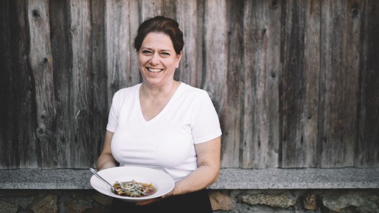Wirtin Doris Schreiber, © Niederösterreich Werbung/Mara Hohla Frau mit weißem T-Shirt hält einen Teller mit Essen vor einer Holzwand.