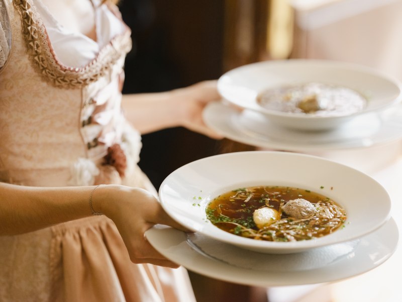 Wachauer Wirtshauskultur, © Niederösterreich Werbung/Michael Reidinger Eine Person in traditioneller Kleidung serviert zwei Suppenteller.