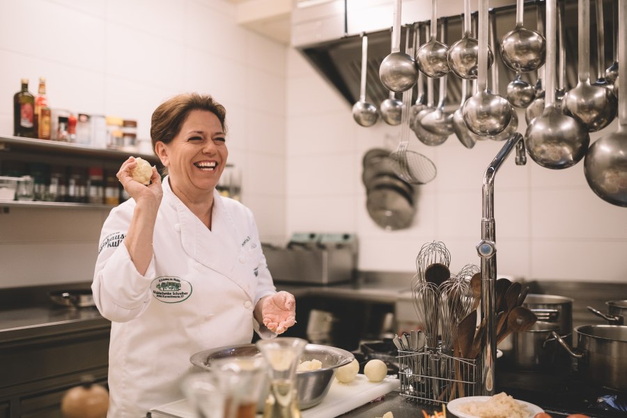 Wirtshausküche mit Waldviertler Karpfen-Haube, © Niederösterreich Werbung/Mara Hohla Eine lachende Köchin in einer professionellen Küche, die einen Teigball in der Hand hält.