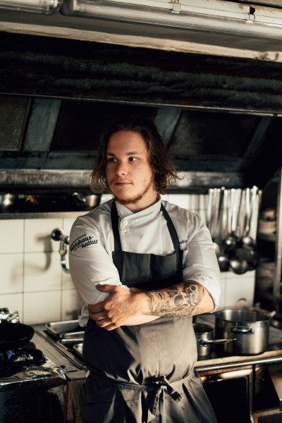 Laurent Amon hat das Zepter von Ulli Amon-Jell übernommen, © Niederösterreich Werbung/Julius Hirtzberger Junger Koch mit Tattoos in einer professionellen Küche, nachdenklich blickend.