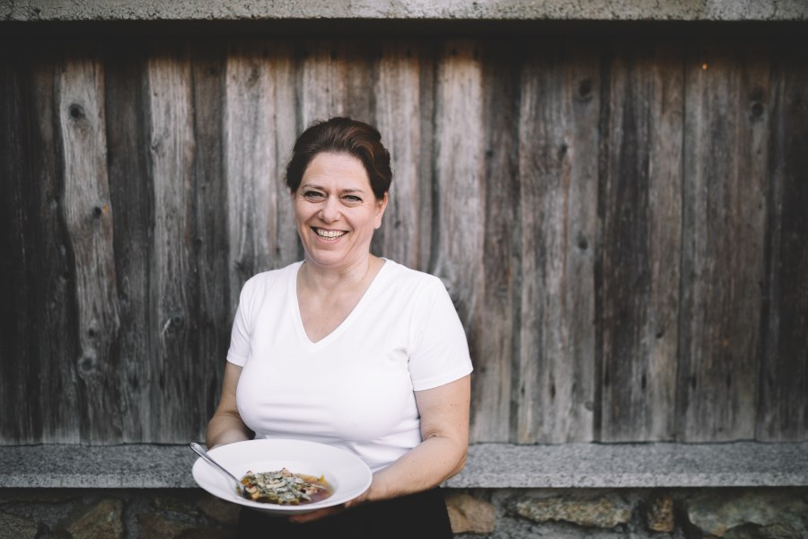 Wirtin Doris Schreiber, © Niederösterreich Werbung/Mara Hohla Frau mit weißem T-Shirt hält einen Teller mit Essen vor einer Holzwand.