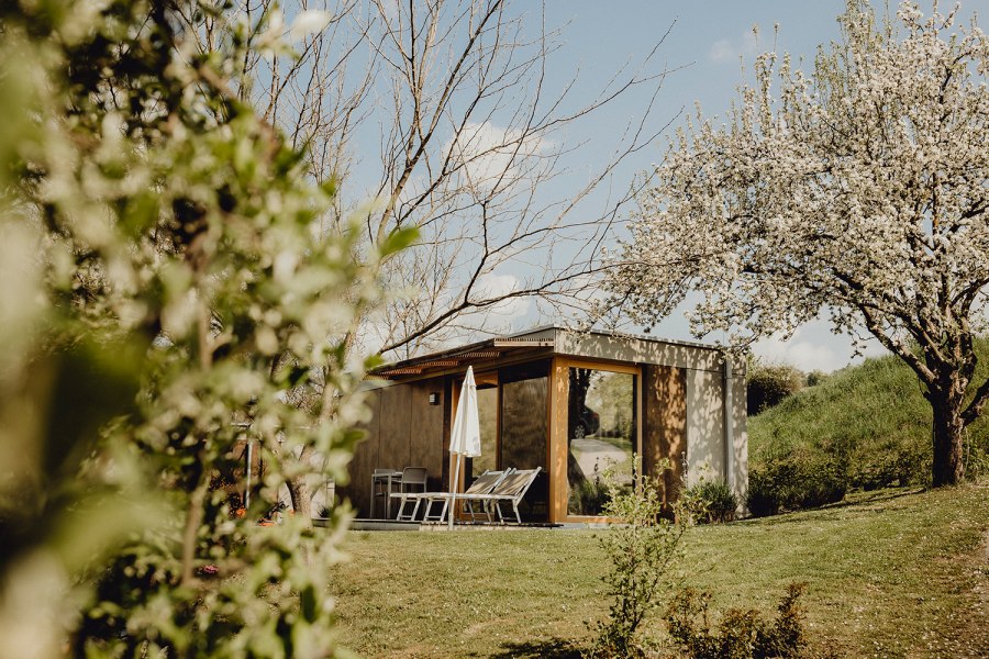 Urlauben im hauseigenen Wiener Alpen Bett, © Niederösterreich Werbung/Sophie Menegaldo Kleines modernes Gebäude in einem Garten mit blühenden Bäumen und Liegestühlen.