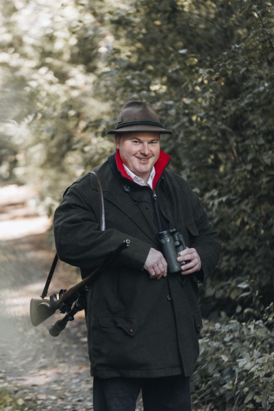 Wirt und Jäger Stephan Solich, © Niederösterreich Werbung/David Schreiber Mann in Jagdkleidung mit Fernglas im Wald.