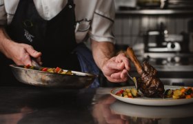 Wirt bietet Kochkurse an, © Niederösterreich Werbung/Daniela Führer Ein Koch in einer professionellen Küche richtet ein Gericht mit Fleisch und Gemüse auf einem Teller an.