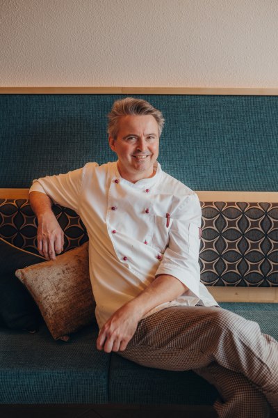 Wirt Hermann Froschauer, © Niederösterreich Werbung/Daniela Führer Ein Mann in Kochkleidung sitzt lächelnd auf einem Sofa.