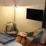 Zimmer mit Bett, Tisch mit zwei Stühlen, Fernseher, Fenster mit blauen Vorhängen und Stehlampe., © Magdalena Donhauser Zimmer mit Bett, Tisch mit zwei Stühlen, Fernseher, Fenster mit blauen Vorhängen und Stehlampe.