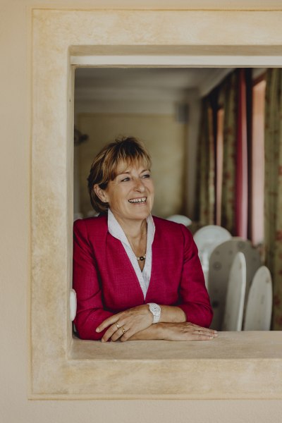 Linde Zimmer, © Landgasthof zur Linde Eine lächelnde Frau in einem roten Blazer lehnt sich durch ein Fenster.