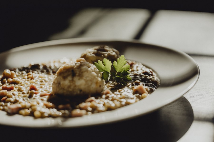 Specklinsen mit Semmelknödel, © Niederösterreich Werbung/Sophie Menegaldo Nahaufnahme eines Tellers mit Linsengericht und Knödeln, garniert mit Petersilie.