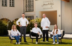 Familie Eisenbock & Chefkoch Christian Schimann, © Niederösterreich Werbung/Andreas Hofer Fünf Personen posieren vor einem Gebäude mit der Aufschrift 'Eisenbock's Strasserhof Hoteleingang'.