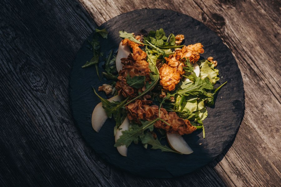 Hühnerfilet, Mandelkruste, Birnen-Most-Salat, © Niederösterreich Werbung/Daniela Führer Hühnerfilet mit Mandelkruste auf Salat mit Birnenscheiben auf einem schwarzen Teller.