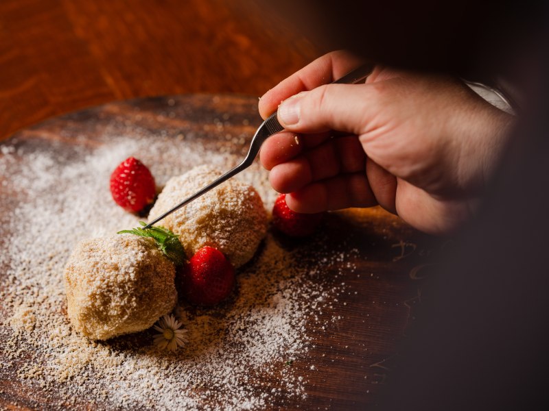 Fruchtige Knödel je nach Saison, © Niederösterreich Werbung/Michael Reidinger Hand dekoriert Dessert mit Erdbeeren und Minze auf Holzplatte.