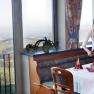 Herrliche Ausblicke erwarten die Gäste, © weinfranz.at Eine Frau deckt einen Tisch in einem Restaurant mit Aussicht auf eine ländliche Landschaft.