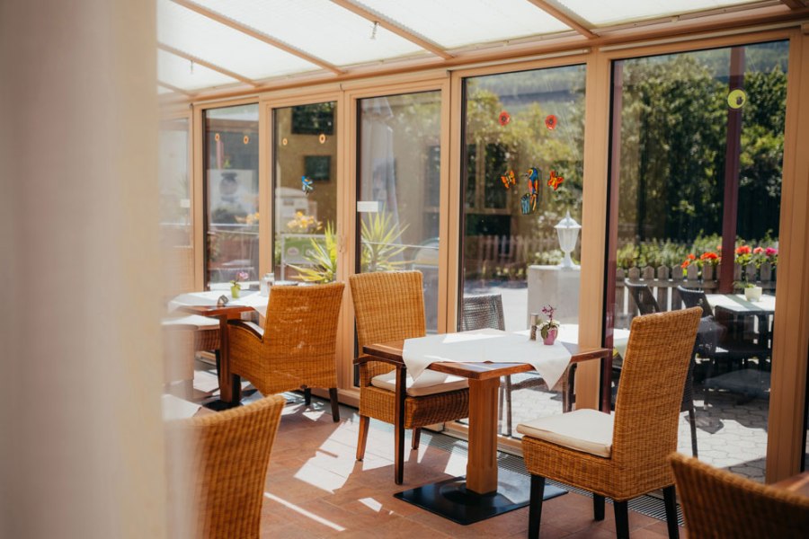 Rastplatz für Wanderer, Druidenweg Ysperklamm, © Niederösterreich Werbung/Daniela Führer Ein heller Wintergarten mit Korbstühlen und gedeckten Tischen, umgeben von großen Fenstern mit Blick ins Grüne.