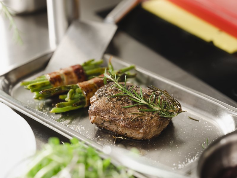 Regionale Fleischqualität & Spezialitätenküche von Spargel bis Kürbis, © Niederösterreich Werbung/Michael Reidinger Ein Steak mit Rosmarin und Bohnen im Speckmantel auf einem Metalltablett.
