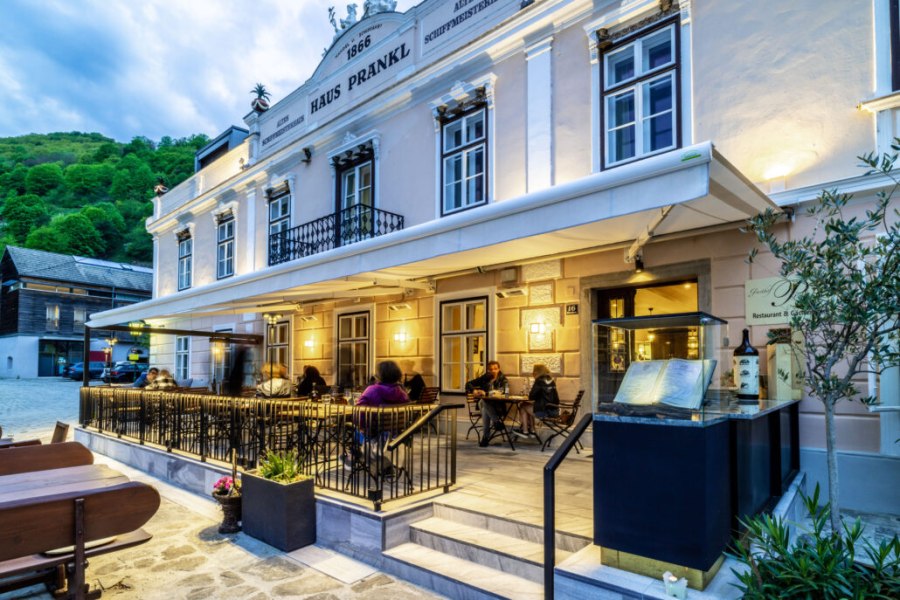 Aussenansicht Gasthof Prankl, © Gasthof Prankl Außenansicht des Gasthofs Prankl mit beleuchteter Terrasse und Gästen an Tischen.