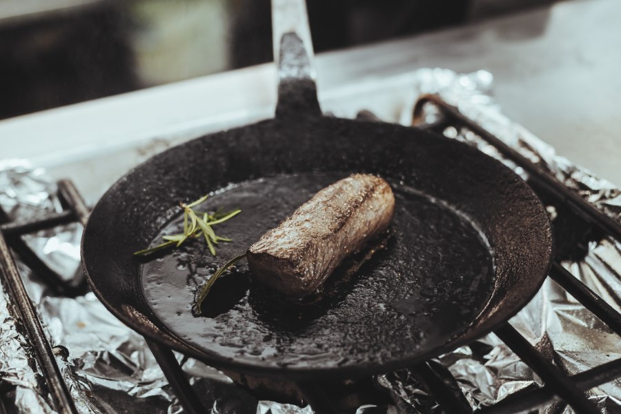 Wildküche: Wurst, Geselchtes, Leberkäse …, © Niederösterreich Werbung/David Schreiber Ein Stück Fleisch brät in einer gusseisernen Pfanne mit Rosmarin.