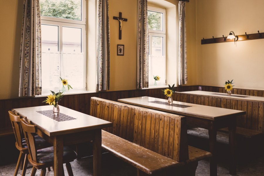 Wo das Dorf zusammen kommt, © Niederösterreich Werbung/David Schreiber Ein rustikaler Raum mit Holzbänken und Tischen, dekoriert mit Sonnenblumen in Vasen. Ein Kreuz hängt an der Wand.